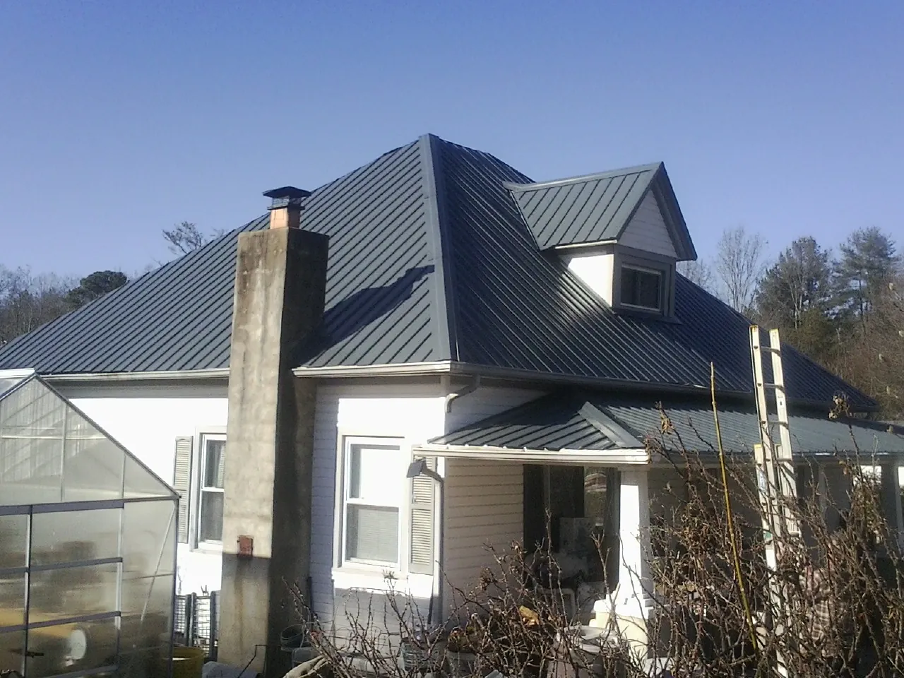 Dark blue standing seam metal roof on a white farmhouse with dormer — Slate & Tile Roof Repair by Roofing Brothers in Larned