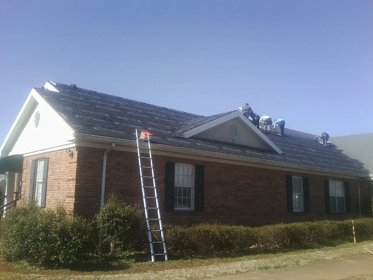 Crew tearing shingles off a brick ranch roof with a ladder set — Metal Roof Repair work by our crew in Larned