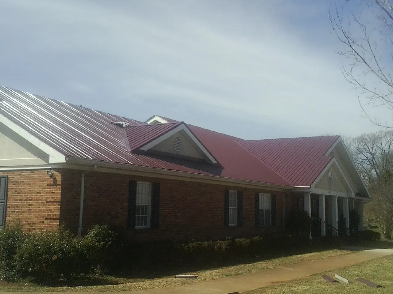 Red metal roof with gabled entries on a long brick building, from a Hail Damage Roof Repair job in Larned