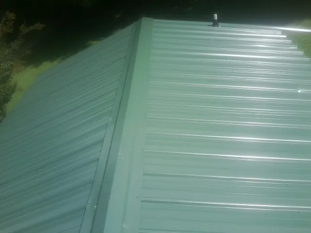 New green metal panels meeting at the ridge of a roof — Flat Roof Repair work by our crew in Larned